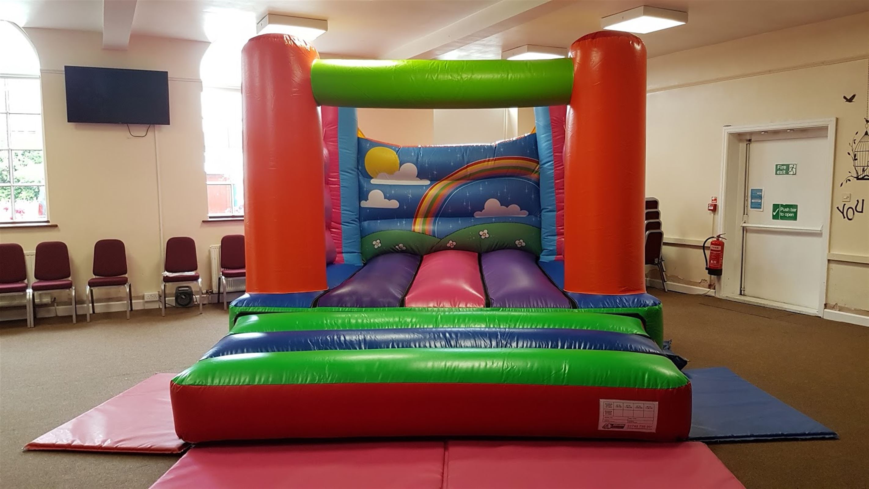 Multi Coloured Rainbow Themed Indoor Bouncy Castle for Hire 14ft x 12ft
