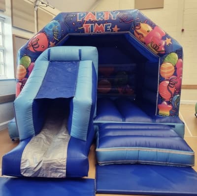 18ft x 12ft Blue Party Time Bouncy Castle With A Front Slide, a bounce and slide combo for hire from Bouncy Castle Factory