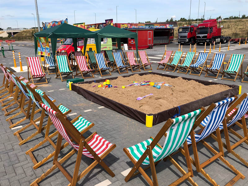 Seaside-themed event setup with a giant sandpit and striped deck chairs